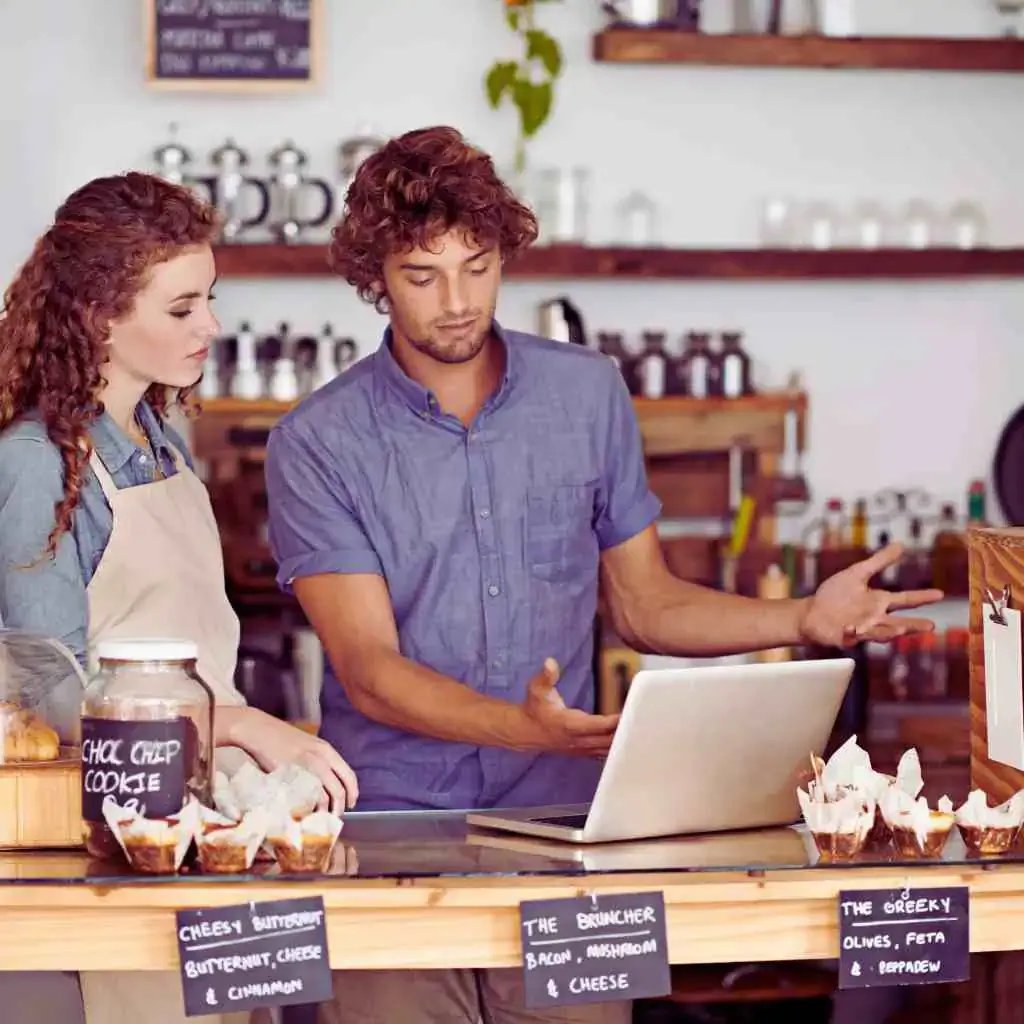 California café owners discussing ADA accessibility requirements on laptop behind bakery counter
