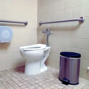 Accessible commercial restroom in California with ADA-compliant toilet, grab bars, and trash bin