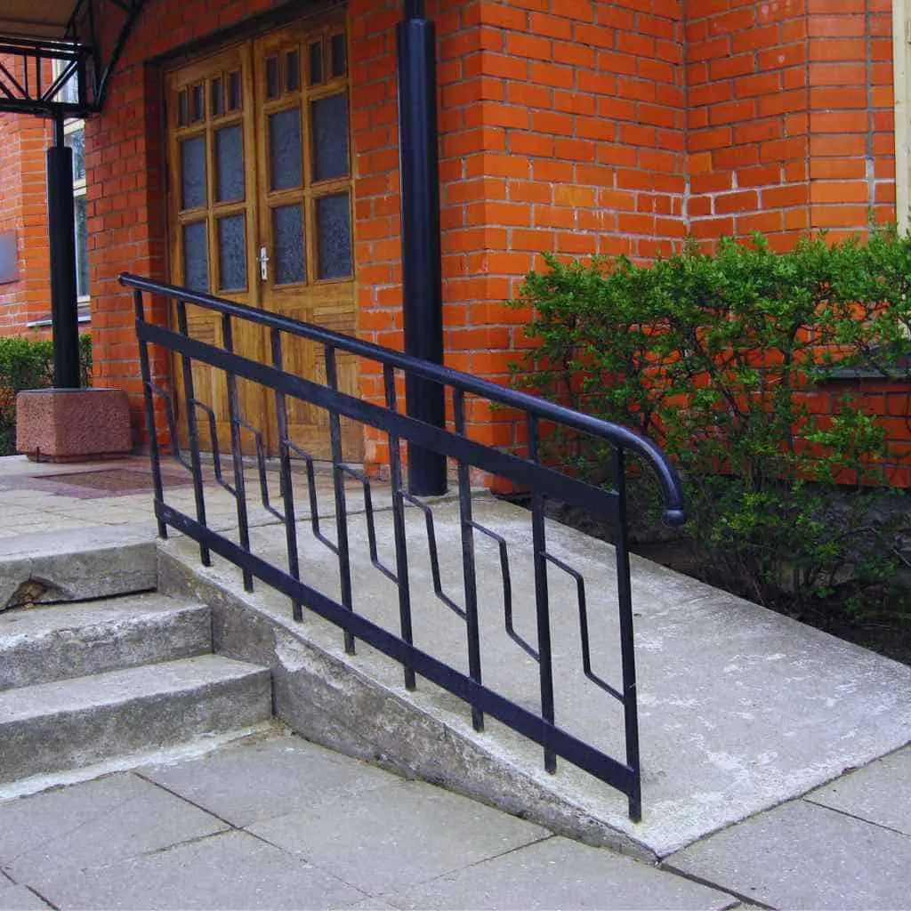 An ADA-compliant concrete ramp with a black steel handrail outside a red-brick building, suitable for wheelchair access in California homes or businesses.