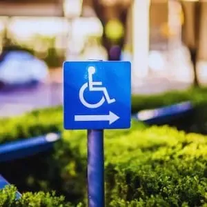 A blue wheelchair accessibility sign with a right-pointing arrow, indicating ADA-compliant sidewalk access in a landscaped California property setting