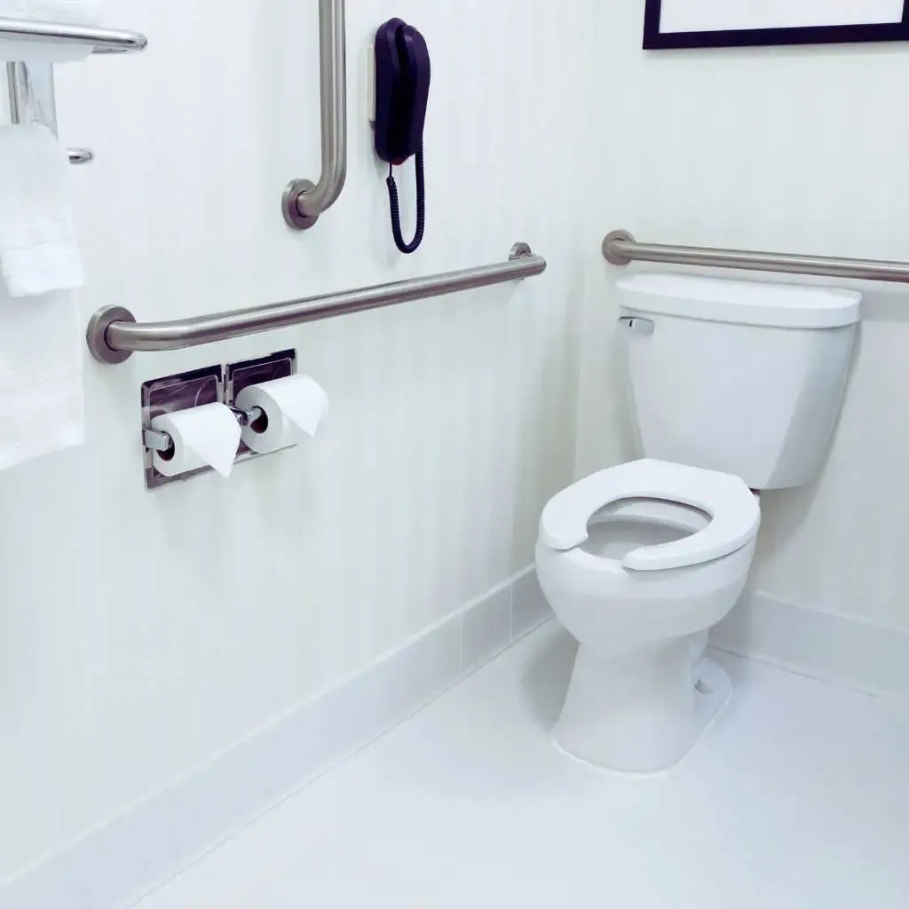 Toilet area in an accessible California restroom showing side and rear grab bars, correct mounting heights, and clear wall space used to illustrate ADA and Title 24 toilet dimension requirements.