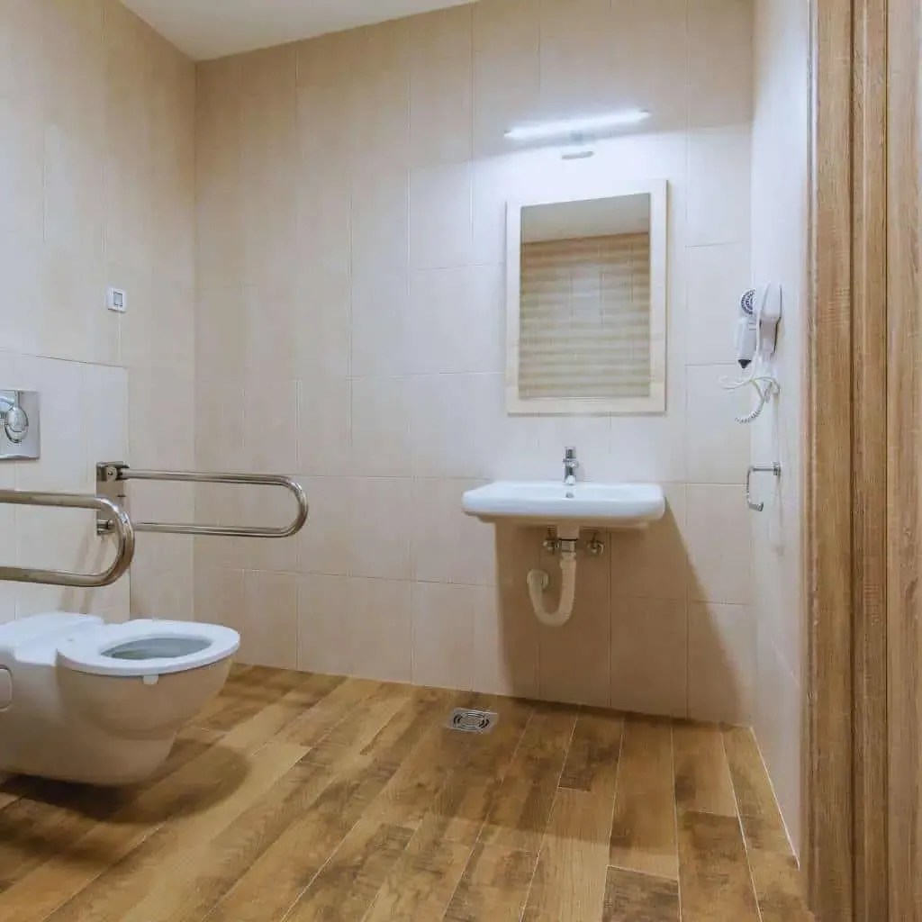 Accessible restroom with wall-mounted toilet, compliant side and rear grab bars, open knee clearance under the sink, and unobstructed maneuvering space consistent with ADA and California Title 24 bathroom dimension requirements.