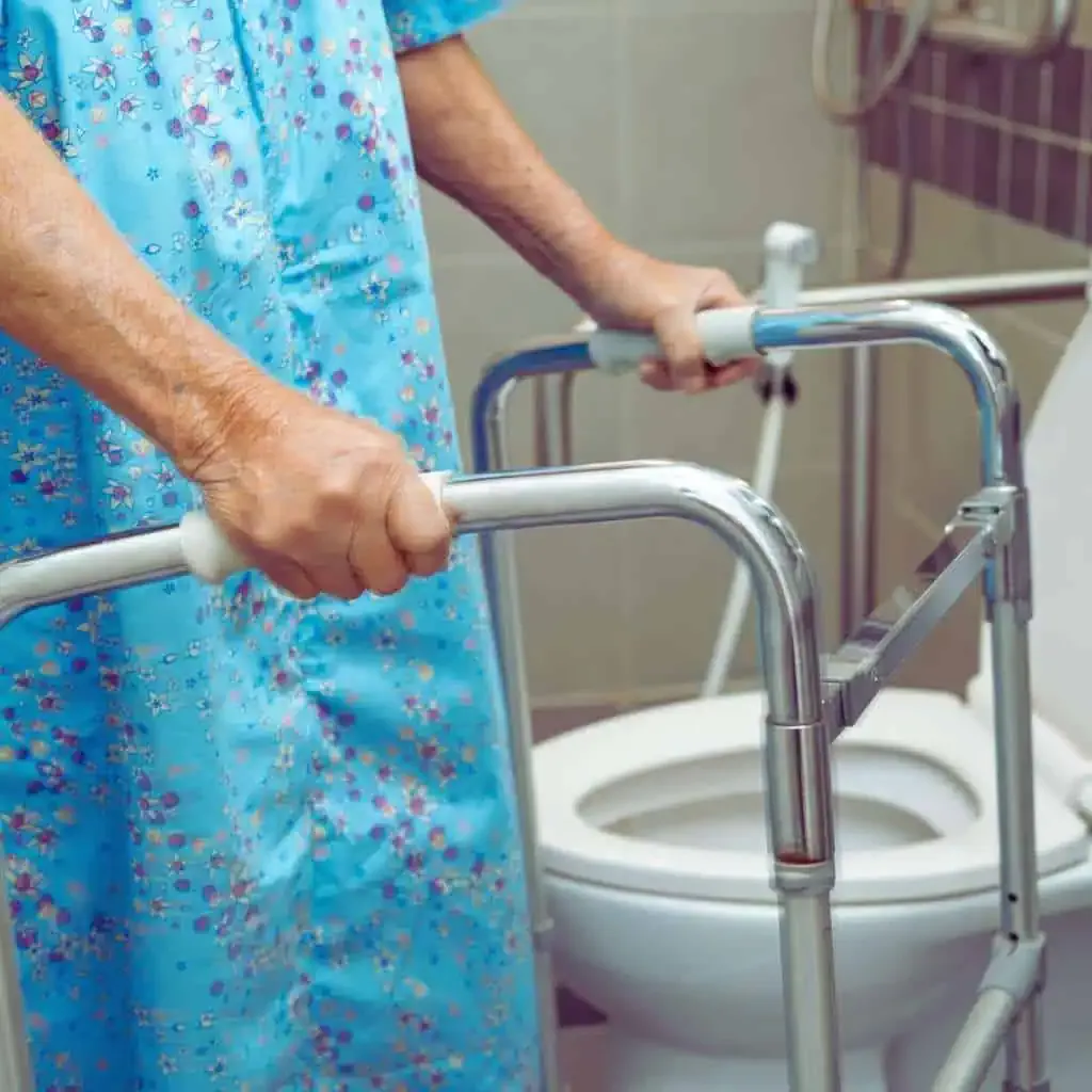 Older adult holding a walker beside a toilet, illustrating the need for adequate ADA and Title 24 clear floor space for safe transfers in accessible bathrooms.